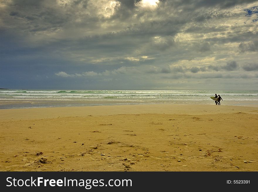 A pair of surfers walk back from the sea before the storm strikes. Space for copy in the sky. A pair of surfers walk back from the sea before the storm strikes. Space for copy in the sky.