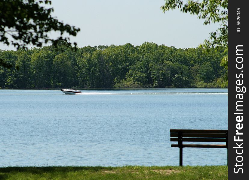 A boat speeding up the lake with a bench in the forefront. A boat speeding up the lake with a bench in the forefront