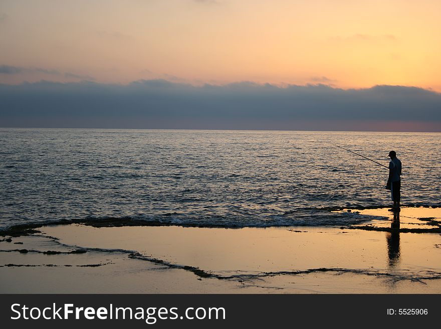 Fisherman on the  seashore at sunset with clouds at the horizon. Fisherman on the  seashore at sunset with clouds at the horizon