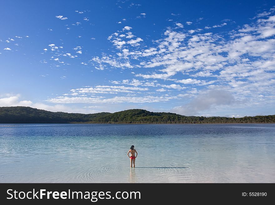 Young girl standing in the tranquil Lake McKanzie in Fraser Island and beautiful blue sky with some nice white clouds.