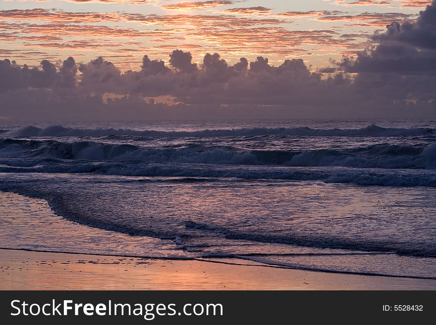 Sunset over a beautiful sandy beach, Very clear and bright perspective with clouds layers that accentuate the horizon, ocean waves are approachind the sandy beach. Sunset over a beautiful sandy beach, Very clear and bright perspective with clouds layers that accentuate the horizon, ocean waves are approachind the sandy beach