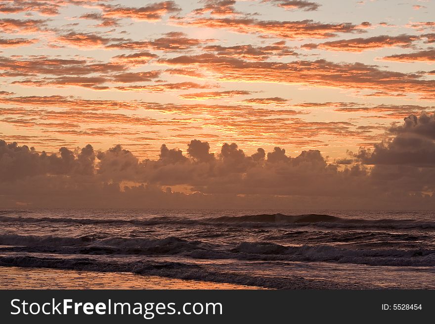 Sunset over a beautiful sandy beach, Very clear and bright perspective with clouds layers that accentuate the horizon, ocean waves are approachind the sandy beach. Sunset over a beautiful sandy beach, Very clear and bright perspective with clouds layers that accentuate the horizon, ocean waves are approachind the sandy beach