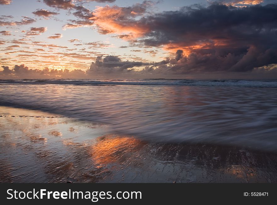 Sunset over a beautiful sandy beach, Very clear and bright perspective with clouds layers that accentuate the horizon, ocean waves are approaching the sandy beach. Sunset over a beautiful sandy beach, Very clear and bright perspective with clouds layers that accentuate the horizon, ocean waves are approaching the sandy beach