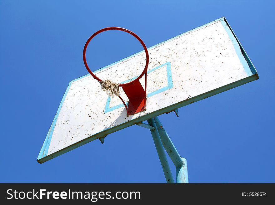 Old basketball hoop on clear blue sky.