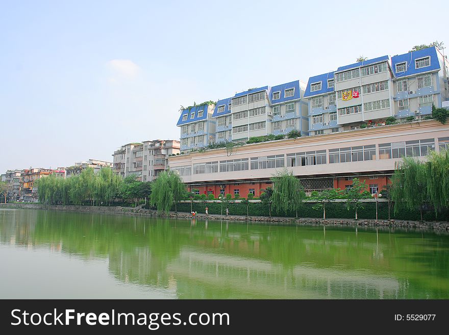 China asia developing city town sky blue cloud lake water reflection tree apartment building pink orange green light waterside lakeside sun sunny sunshine shining lovely