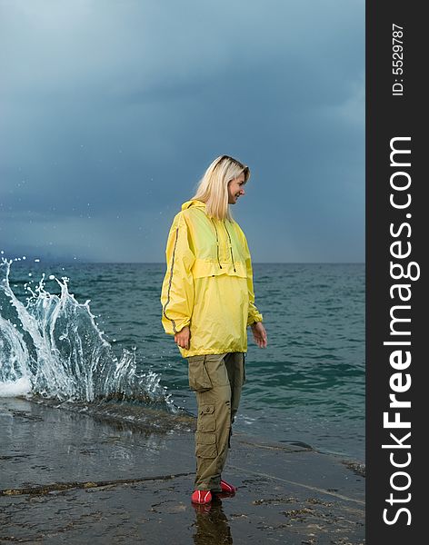 Young woman in yellow raincoat near the ocean at storm