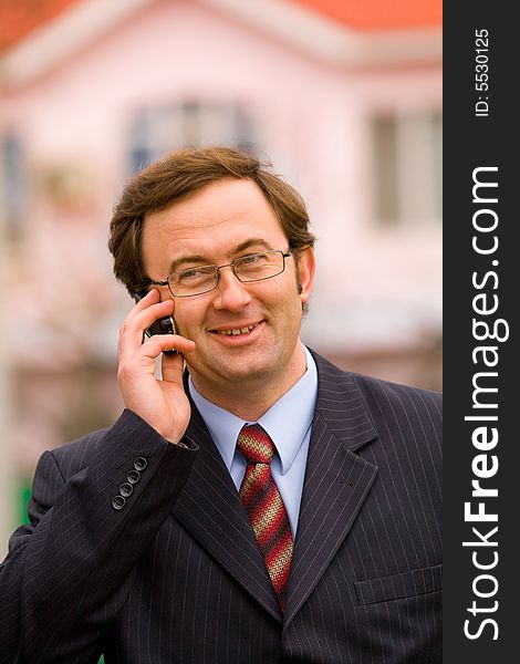 Businessman talking by mobile phone over blurred house background. Businessman talking by mobile phone over blurred house background
