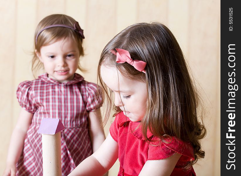 Portrait of two little girls building toy tower from wooden bricks at home