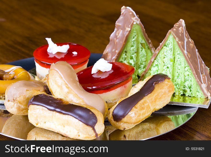 Assortment of freshly baked cakes on silver reflective plate on wooden table. Assortment of freshly baked cakes on silver reflective plate on wooden table