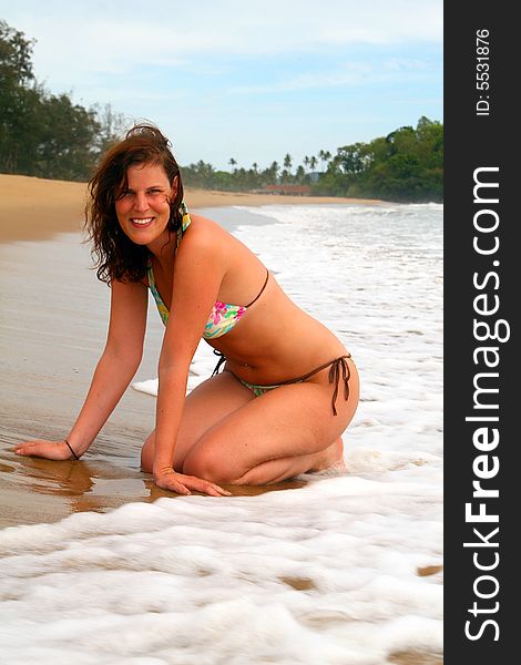 A young woman at the beach in the water. Sitting in the sand with a bikini. Ideal Vacation shot. A young woman at the beach in the water. Sitting in the sand with a bikini. Ideal Vacation shot.