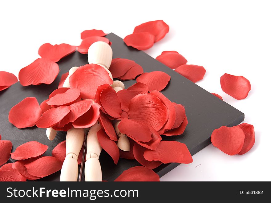 A wooden man lying on a black border mirror with red rose petal around. A wooden man lying on a black border mirror with red rose petal around