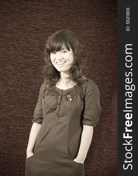 A cute asian girl wears a brown skirt with her hands put in pocket. She offers a big and sweet smile!