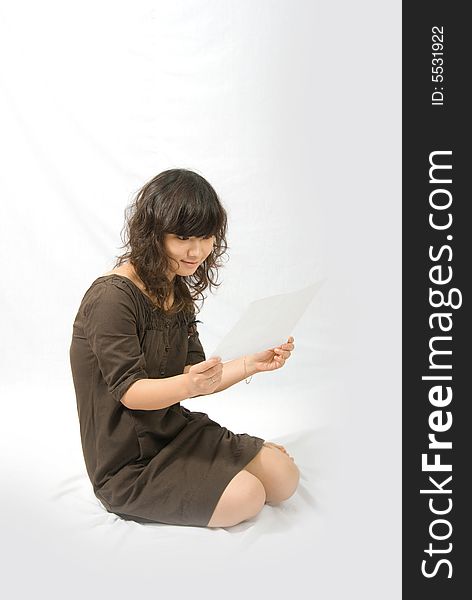 A cute asian girl wears a brown skirt is reading a paper white sitting on the white ground. A cute asian girl wears a brown skirt is reading a paper white sitting on the white ground