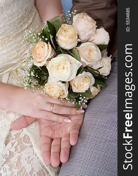 Hands of a newly-married couple with a bouquet, close up