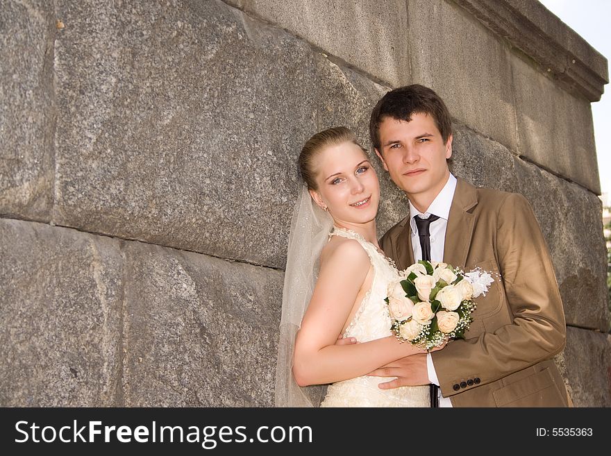 Newly-married couple near a stone wall