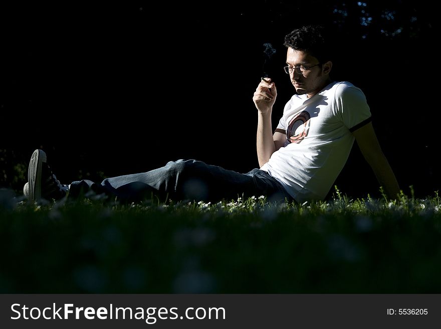 Young man sitting on grass in a park and smoking. Young man sitting on grass in a park and smoking.