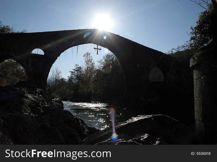 Old stone bridge with cross, over a river,