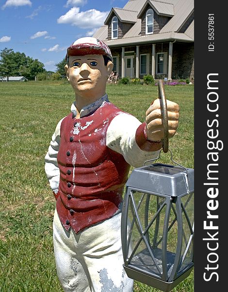 Lawn statue holding lantern in front yard of house with blue sky. Lawn statue holding lantern in front yard of house with blue sky