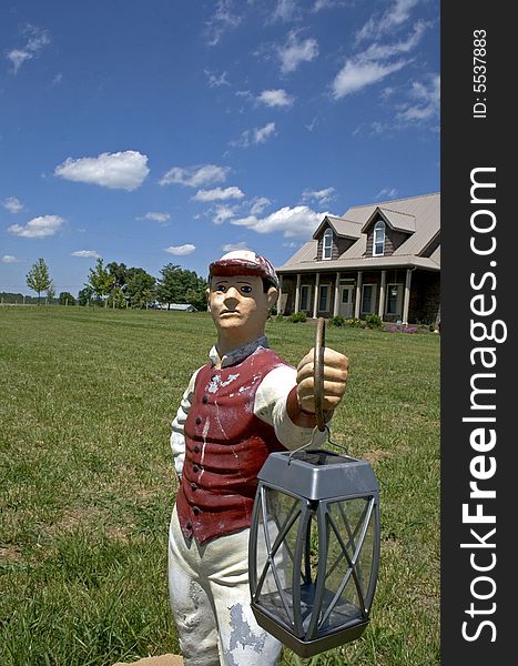 Lawn statue holding lantern in front yard of house with blue sky. Lawn statue holding lantern in front yard of house with blue sky