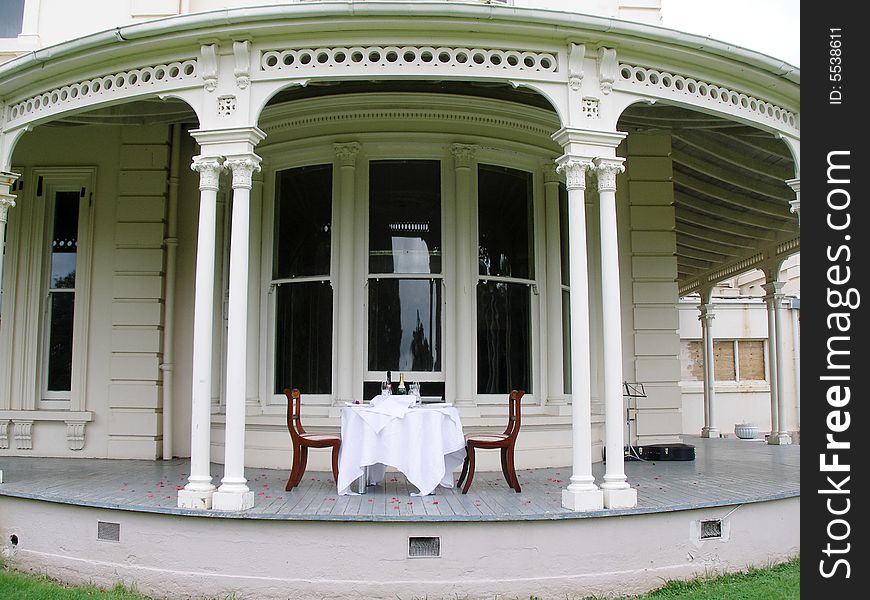 Romantic dining experience in front of antique mansion with white tablecloth, rose petals and wine. Romantic dining experience in front of antique mansion with white tablecloth, rose petals and wine.