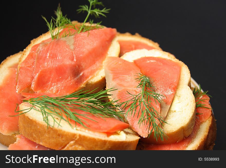 Sandwiches with slices of a salmon, a butter and fennel on a dark background.