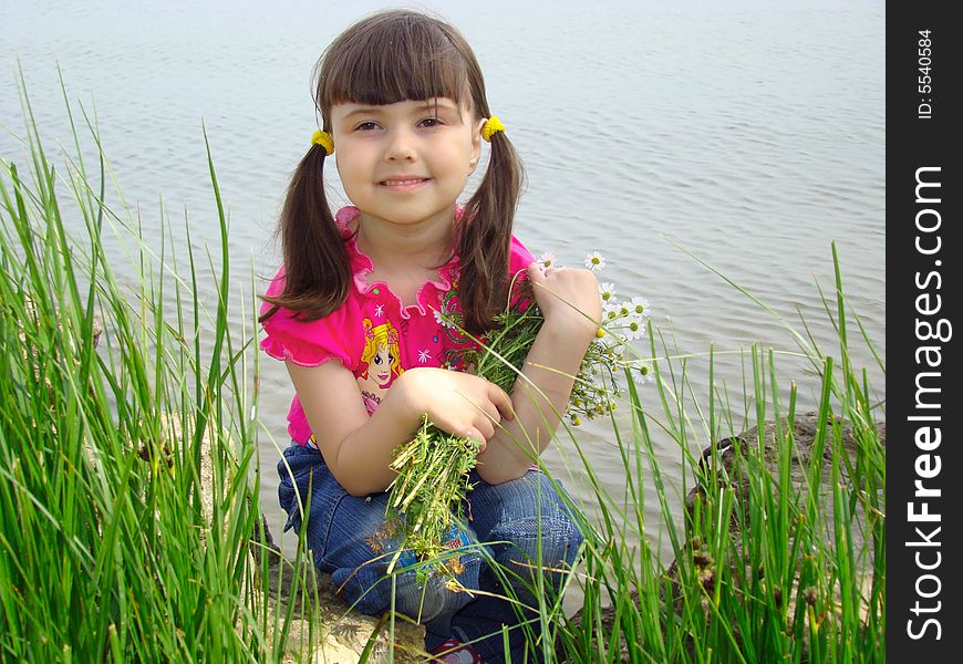 Little girl with the bouquet of camomiles on the riverside. Little girl with the bouquet of camomiles on the riverside.