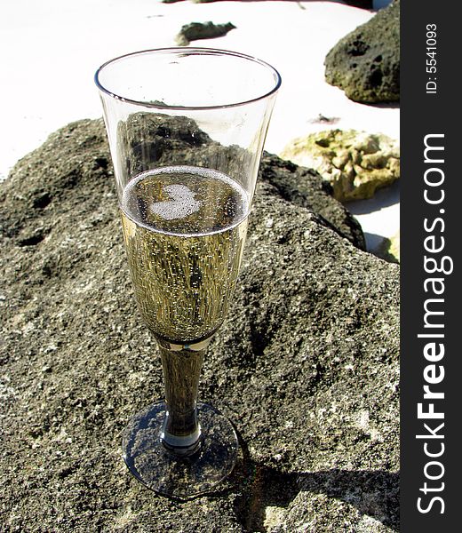 Glass of champage balancing on rocks on the beach. Glass of champage balancing on rocks on the beach