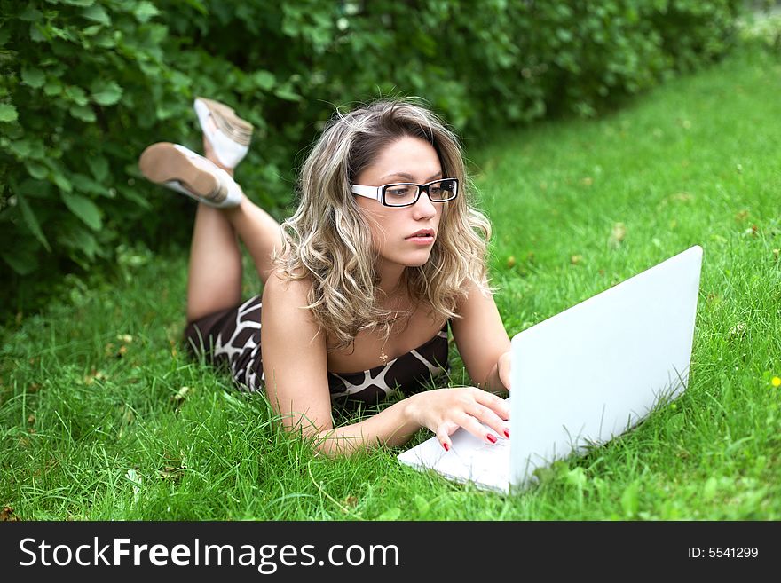 Girl with white laptop lying on green grass background. Girl with white laptop lying on green grass background