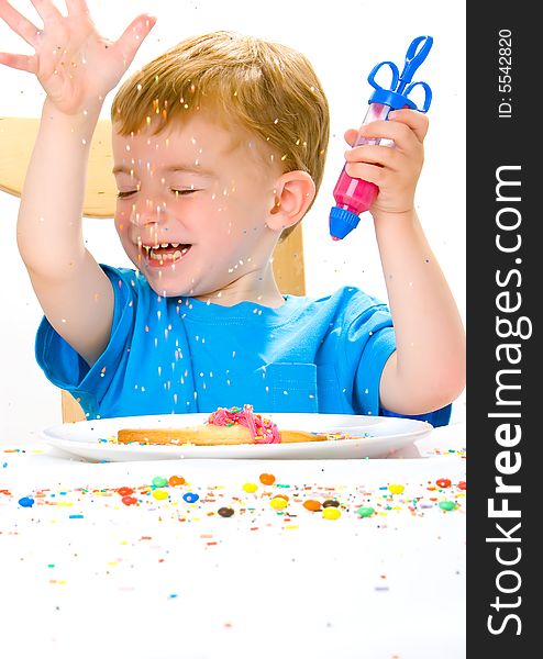 Three year old boy in blue top decorating biscuits with pink icing and sweets. Three year old boy in blue top decorating biscuits with pink icing and sweets
