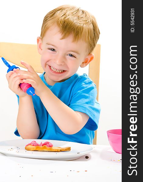 Three year old boy in blue top decorating biscuits with pink icing and sweets. Three year old boy in blue top decorating biscuits with pink icing and sweets