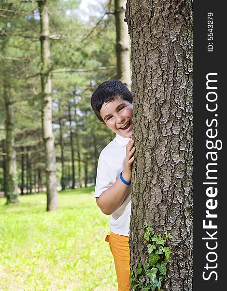 Portrait of young happy boy behind tree at park. Portrait of young happy boy behind tree at park.