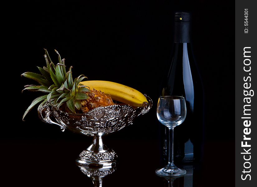 Vase with fruit, a bottle and a glass on a black background. Vase with fruit, a bottle and a glass on a black background