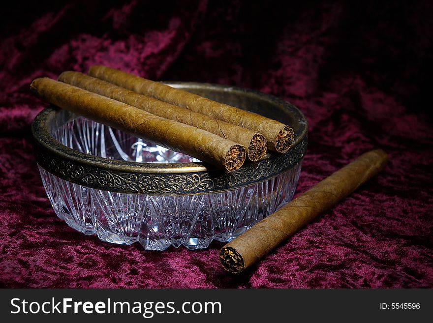 Four cigars on a glass ashtray, crimson velvet background