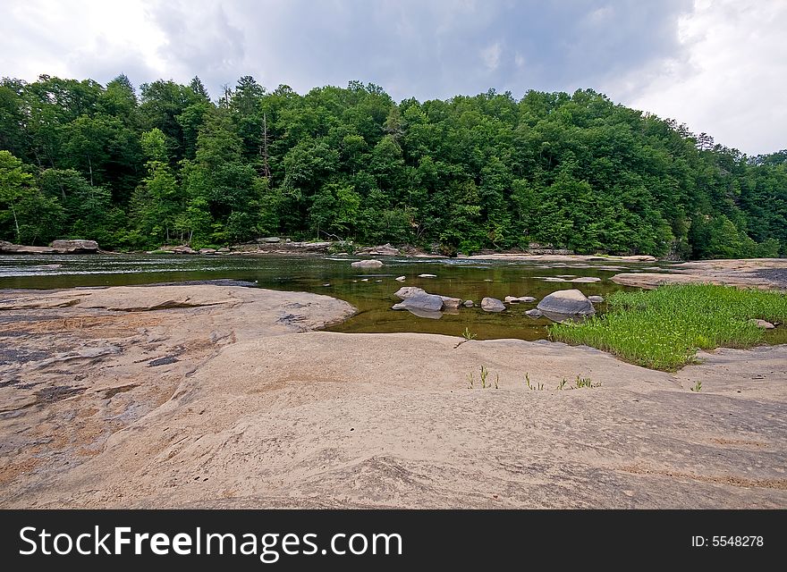 A rocky river shore with woods in the background