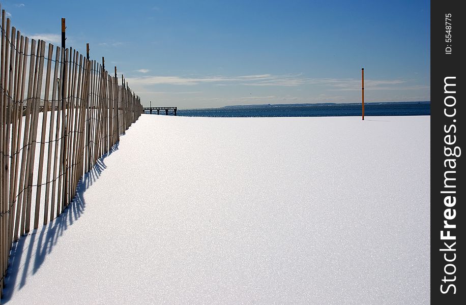 Fence, snow, post, dark blue ocean and gulls in the distance. Fence, snow, post, dark blue ocean and gulls in the distance