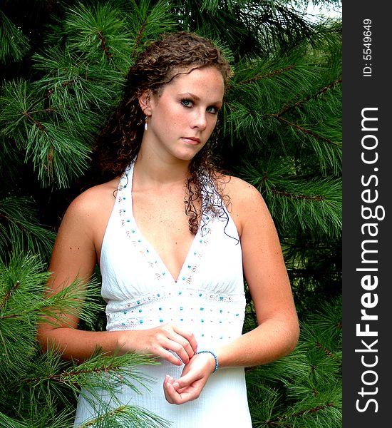 Young woman standing among pine trees in white dress with turquoise trim. Young woman standing among pine trees in white dress with turquoise trim