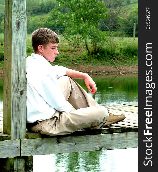 Teenage boy sitting on pier looking into the water on cloudy morning. Teenage boy sitting on pier looking into the water on cloudy morning