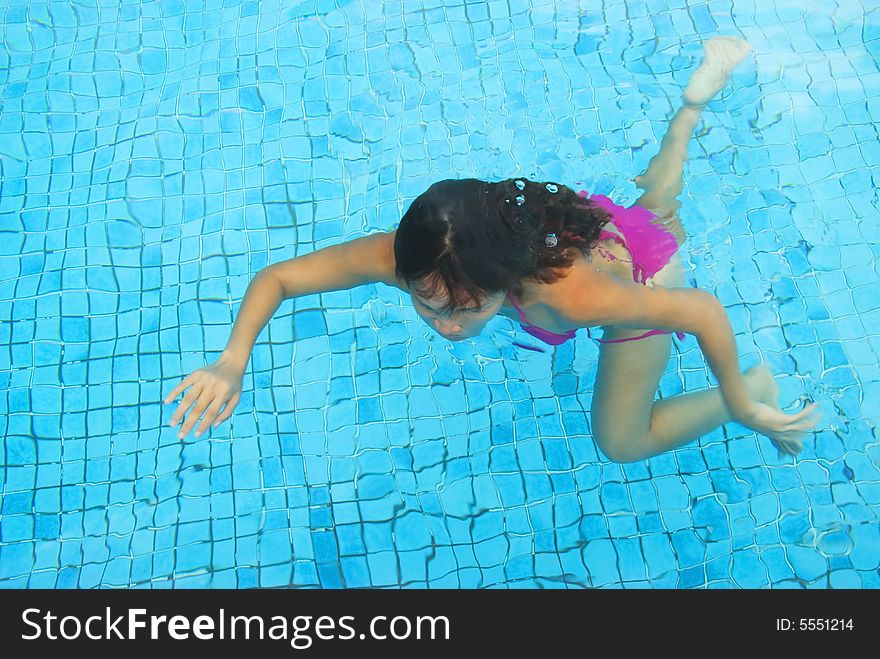 A young woman wearing a pink bikini swimming in a pool. A young woman wearing a pink bikini swimming in a pool