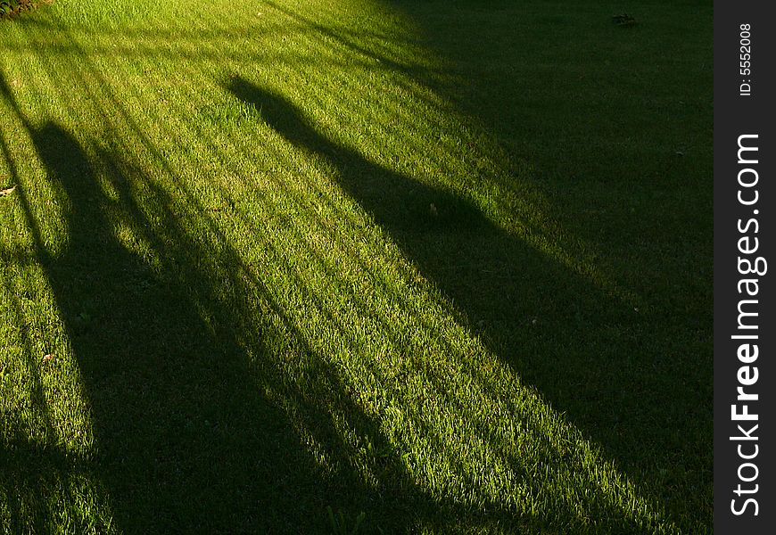 The shadows of two people behind a fence on a plain lawn. The shadows of two people behind a fence on a plain lawn