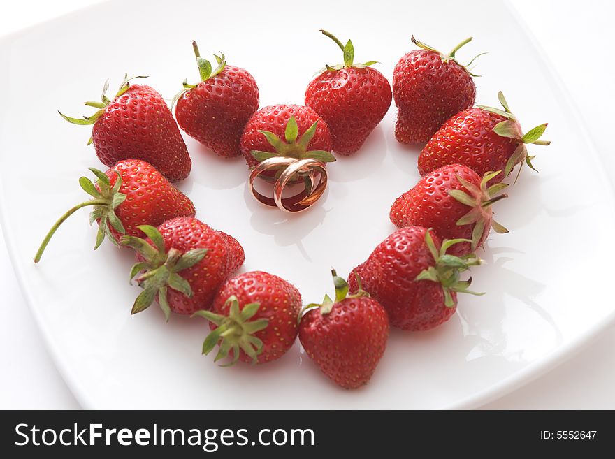 Wedding rings inside strawberry heart on a white plate