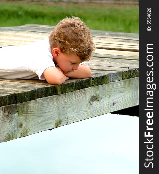 Boy lying on pier looking into water on a cloudy day. Boy lying on pier looking into water on a cloudy day