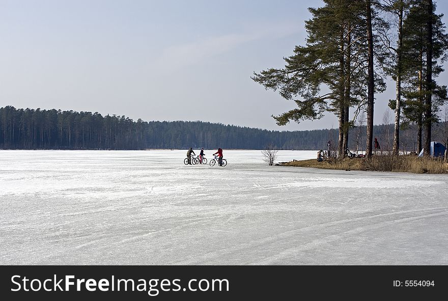 Bicyclists on ice of forest lake in april