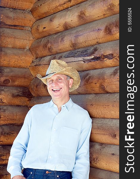 Laughing man in cowboy hat leaning against a log cabin. Verictally framed photograph. Laughing man in cowboy hat leaning against a log cabin. Verictally framed photograph