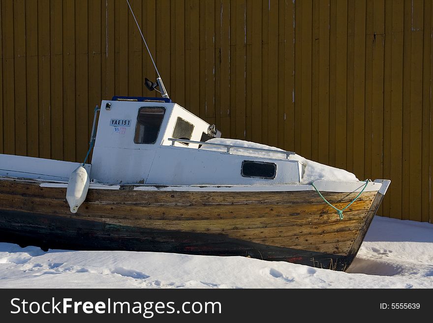 Boat in the snow in front of wall of wood