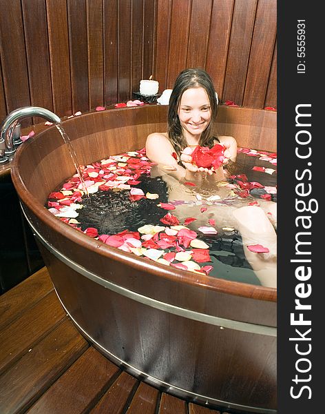 A young girl in a tub of water, holding various rose petals. - vertically framed. A young girl in a tub of water, holding various rose petals. - vertically framed