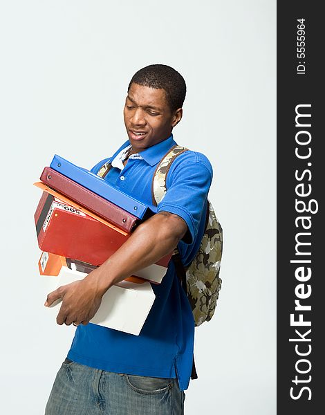 Male student wearing a backpack carries notebooks and boxes. He looks frustrated. Vertically framed photograph. Male student wearing a backpack carries notebooks and boxes. He looks frustrated. Vertically framed photograph.