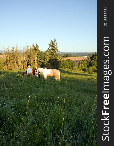 Two farmers smiling for the camera in front of trees as their horses are near them on a grassy hill. - vertically framed. Two farmers smiling for the camera in front of trees as their horses are near them on a grassy hill. - vertically framed