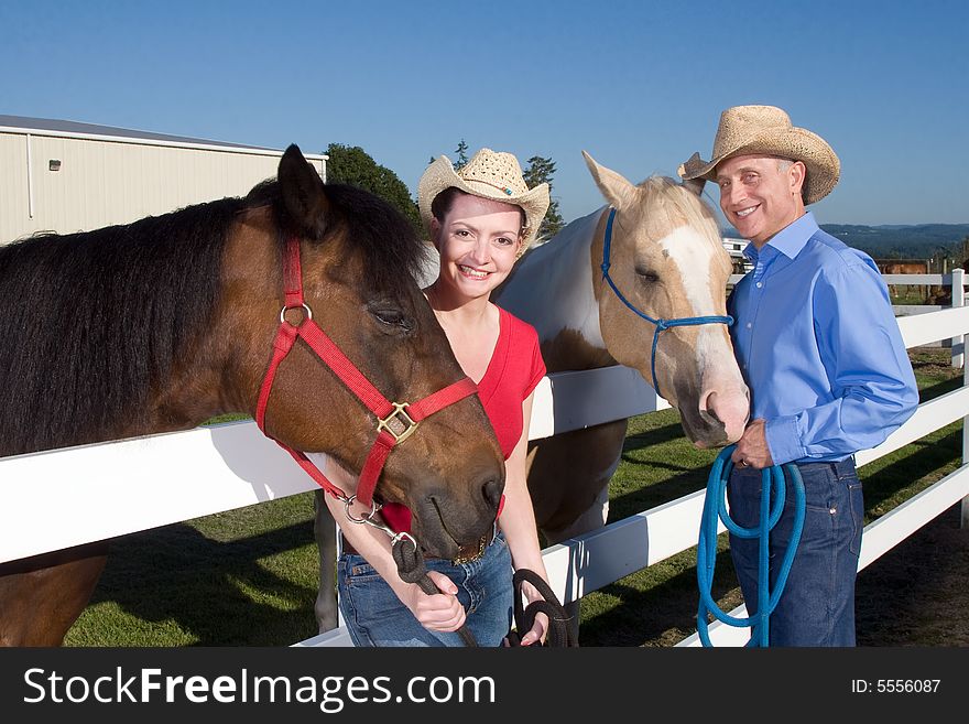 Smiling couple wearing cowboy hats stand next to their horses. Horizontally framed photograph. Smiling couple wearing cowboy hats stand next to their horses. Horizontally framed photograph.
