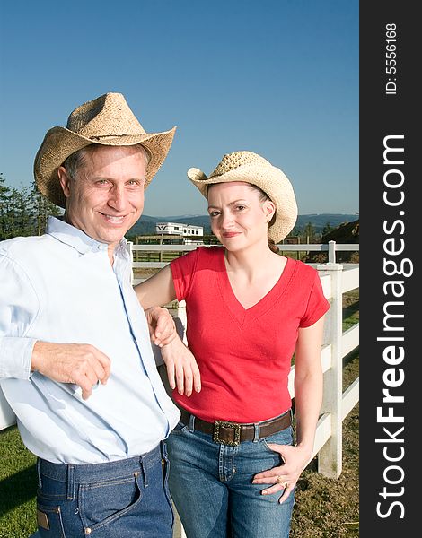 Smiling cowboy and cowgirl leaning against a fence. Vertically framed photograph. Smiling cowboy and cowgirl leaning against a fence. Vertically framed photograph.