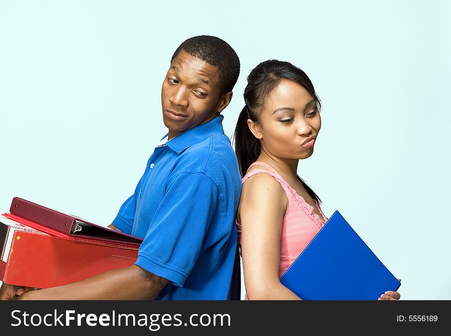 Two students standing back to back carrying books. They look frustrated. Horizontally framed photograph. Two students standing back to back carrying books. They look frustrated. Horizontally framed photograph.